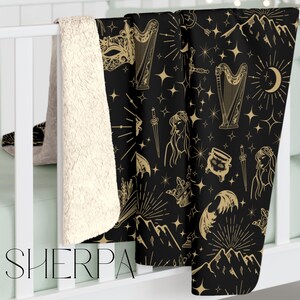 Fantasy inspired blanket with a celestial print in tan on a black blanket, the pattern includes images of moons, masks, bat wings, books, harp, fae and stars for fans of acotar and sarah j maas