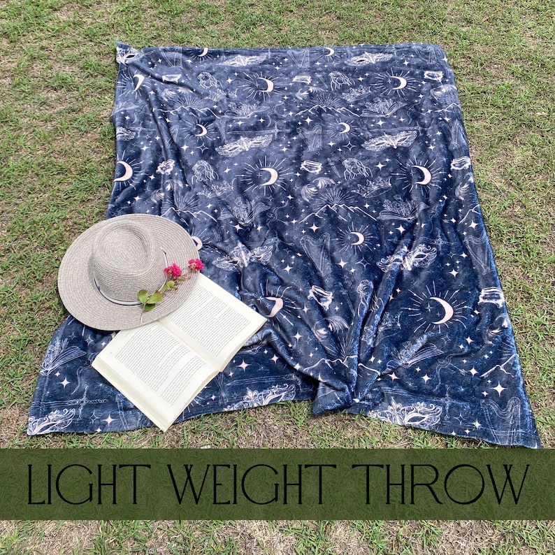 Fantasy inspired blanket with a celestial print in tan on a black blanket, the pattern includes images of moons, masks, bat wings, books, harp, fae and stars for fans of acotar and sarah j maas