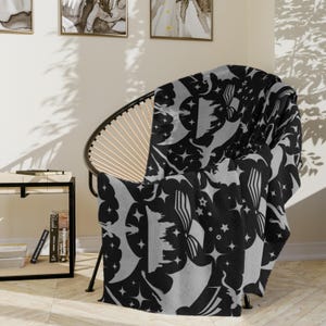 May include: A black and gray throw blanket with a repeating pattern of stars, moons, and stylized clouds. The blanket is draped over a chair.
