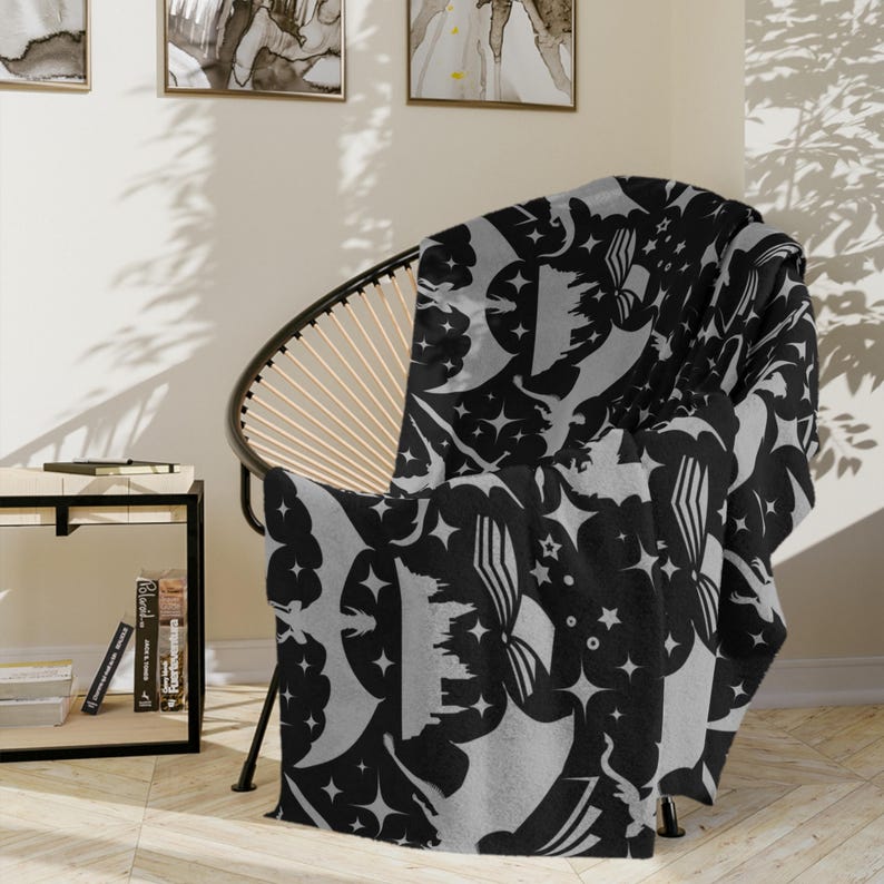 May include: A black and gray throw blanket with a repeating pattern of stars, moons, and stylized clouds. The blanket is draped over a chair.