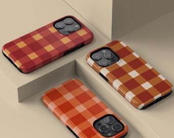 May include: Three phone cases with a plaid pattern in shades of red, orange, and brown. The cases have a glossy finish and a black border. The cases are arranged on a neutral-colored surface.
