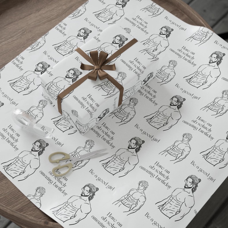 May include: A wrapped gift with a brown ribbon and bow sits on wrapping paper. The paper features a repeating pattern of a muscular man illustration with the phrases "Have an absolutely amazing birthday" and "Be a good girl."