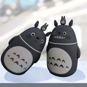 Op de afbeelding: Twee zwarte en grijze keramische bekers met een cartoonfiguurontwerp. De bekers hebben een grijs en wit patroon op de onderste helft en een zwart cartoonfiguur op de bovenste helft. Het figuur heeft grote oren en een kleine mond.