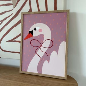 May include: A framed illustration of a white swan with a pink bow on a pink background with white polka dots.