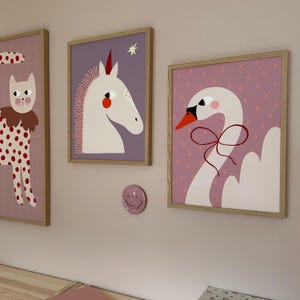 May include: Three framed illustrations on a pink wall. The illustrations feature a white cat with red polka dots, a white unicorn with a red star, and a white swan with a red bow.