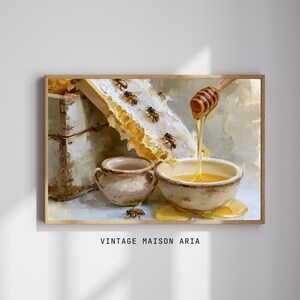 Könnte beinhalten: Ein Ölgemälde-Druck mit einem hölzernen Bienenstock, einem Stück goldenem Bienenwaben mit Bienen und einer Keramikschale voller Honig, aus der Honig mit einem Holzlöffel geträufelt wird. Der Text VINTAGE MAISON ARIA steht unten auf dem Bild.