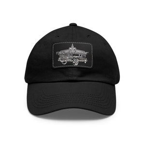 Op de afbeelding: Zwarte baseballpet met een zilveren patch met een auto en de tekst "The Box Chevy Movement".
