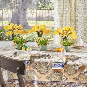 May include: A dining table set for a spring celebration. The table is covered with a patterned tablecloth and set with plates, silverware, napkins, and small vases of yellow flowers. Easter eggs and small potted plants are also present.