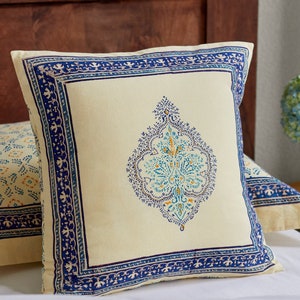 May include: A cream-colored throw pillow with a blue and yellow floral pattern. The pillow has a blue border with a decorative design.