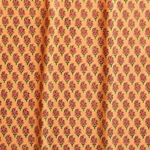 May include: A close-up of a fabric with a repeating pattern of pink and green floral motifs on a light orange background.