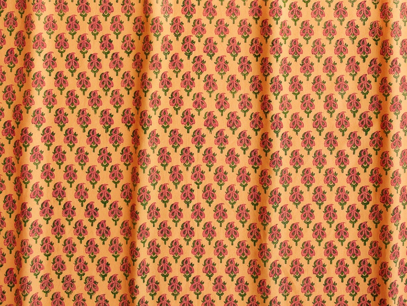 May include: A close-up of a fabric with a repeating pattern of pink and green floral motifs on a light orange background.