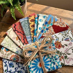 May include: A collection of square fabric napkins featuring diverse floral and geometric block-print patterns in vibrant colors including blue, red, yellow, and green, neatly stacked and tied together with a natural jute twine bow.