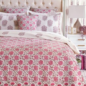 K&ouml;nnte beinhalten: Ein wei&szlig;er Bettbezug mit einem rosafarbenen Blumenmuster. Der Bettbezug hat einen wei&szlig;en Rand mit einem rosafarbenen und grauen Blumendesign. Der Bettbezug liegt auf einem Bett mit wei&szlig;en Kissen und einem wei&szlig;en Kopfteil.