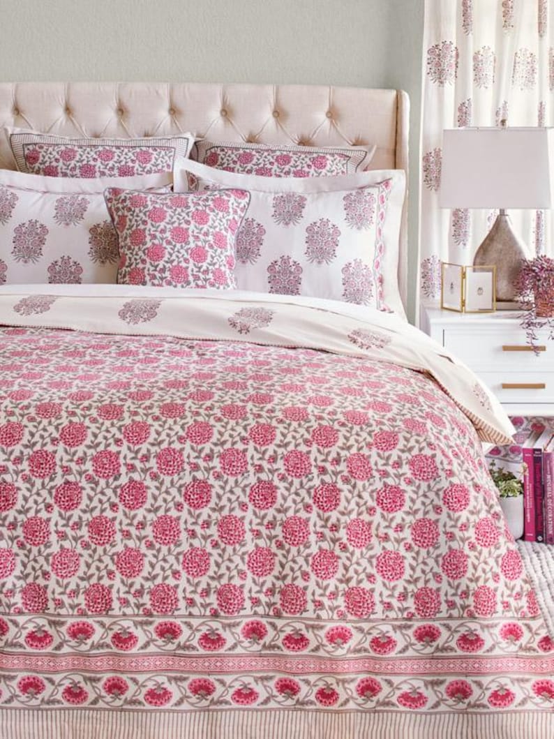 K&ouml;nnte beinhalten: Ein wei&szlig;er Bettbezug mit einem rosafarbenen Blumenmuster. Der Bettbezug hat einen wei&szlig;en Rand mit einem rosafarbenen und grauen Blumendesign. Der Bettbezug liegt auf einem Bett mit wei&szlig;en Kissen und einem wei&szlig;en Kopfteil.