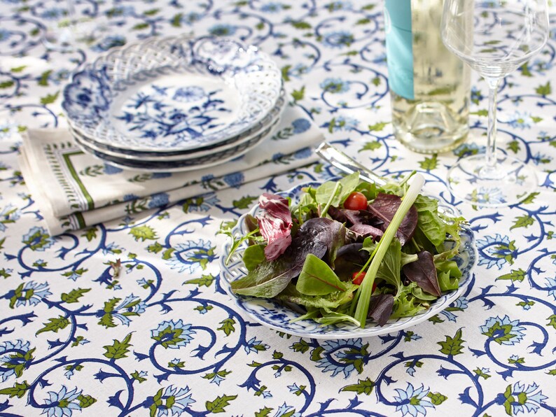 K&ouml;nnte beinhalten: Eine wei&szlig;e Tischdecke mit einem blauen und gr&uuml;nen Blumenmuster. Ein wei&szlig;er Teller mit einem blauen und gr&uuml;nen Blumenmuster steht auf dem Tisch. Ein Salat mit gr&uuml;nem Salat, roten Tomaten und gr&uuml;nen Zwiebeln liegt auf dem Teller.