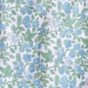 Op de afbeelding: Witte stof met een herhalend patroon van blauwe bloemen, groene bladeren en witte vogels. Het patroon is in traditionele stijl.