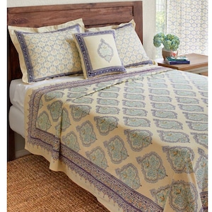 May include: A cream-colored bedspread with a blue and green paisley pattern. The bedspread has a decorative border with a blue and purple floral design. The bedspread is on a bed with two pillows, one with a blue and white paisley pattern and the other with a cream-colored floral design.