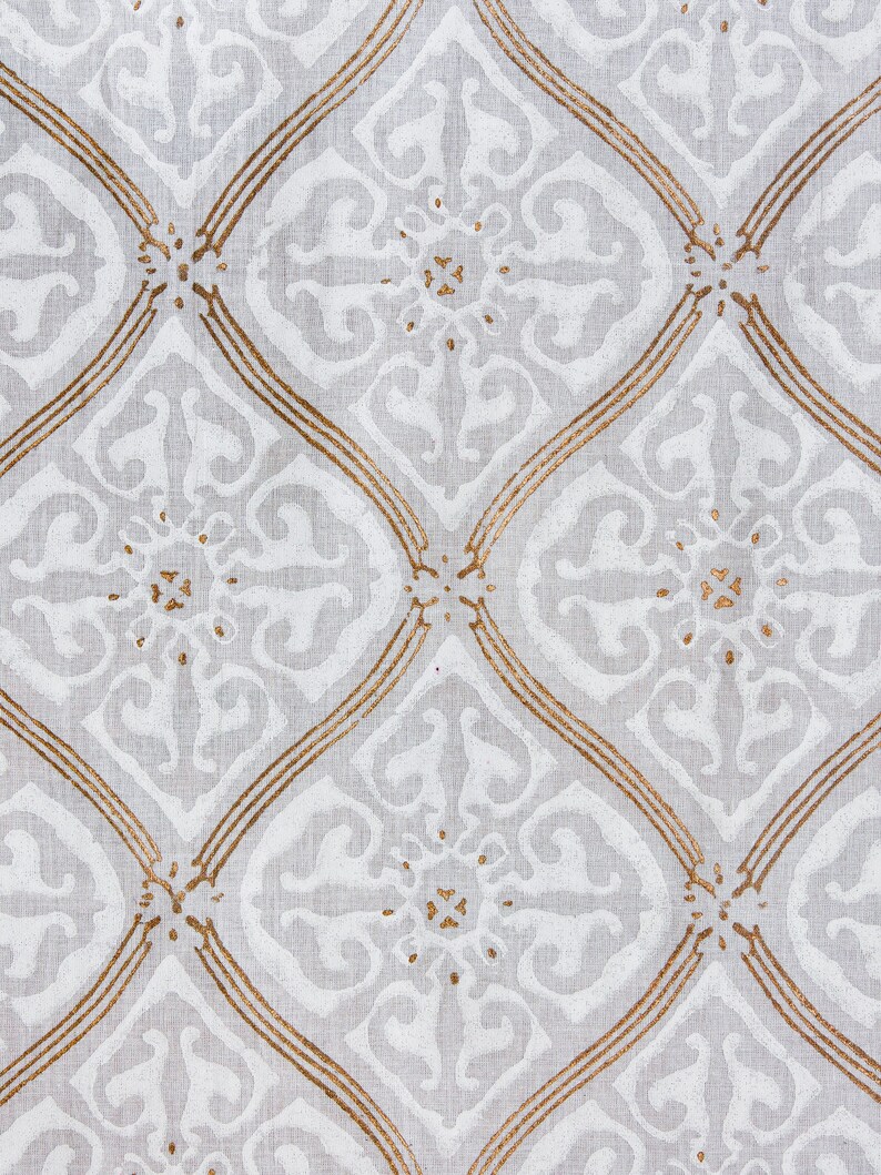 May include: White fabric with a repeating pattern of gold-colored diamond shapes and floral designs.