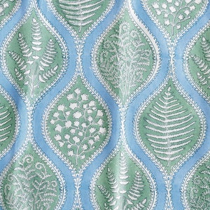 Op de afbeelding: Een blauwe en groene stof met een herhalend patroon van gestileerde varenbladeren en bloemen. Het patroon heeft een traanvorm met een witte omtrek.