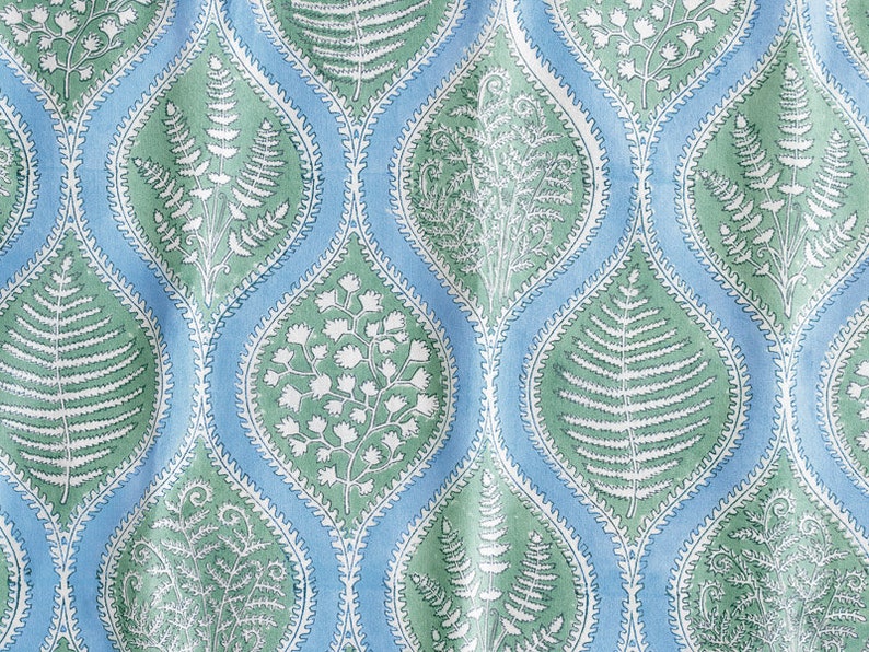 Op de afbeelding: Een blauwe en groene stof met een herhalend patroon van gestileerde varenbladeren en bloemen. Het patroon heeft een traanvorm met een witte omtrek.