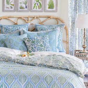 May include: A bedroom scene featuring a bed with a woven headboard and bedding in shades of blue and green. The bedding has a botanical pattern. Above the bed are four framed botanical prints. A matching curtain and a lamp complete the decor.