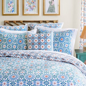 May include: A white bed with a blue and orange patterned duvet cover and matching pillowcases. The bed has a wooden headboard and is decorated with framed artwork.