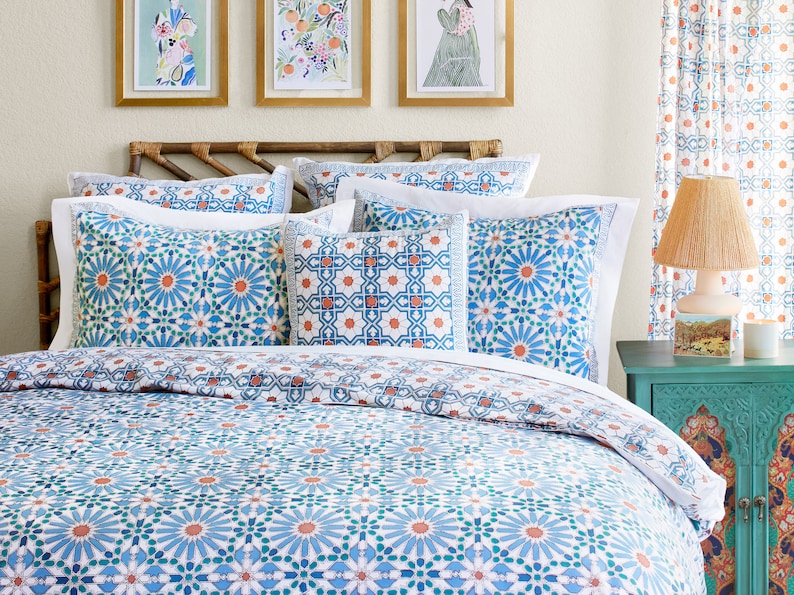 May include: A white bed with a blue and orange patterned duvet cover and matching pillowcases. The bed has a wooden headboard and is decorated with framed artwork.