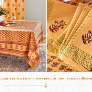May include: A yellow tablecloth with a floral print and a matching set of napkins. The tablecloth has a border with a repeating pattern of flowers and leaves. The napkins have a similar floral print with a green border.