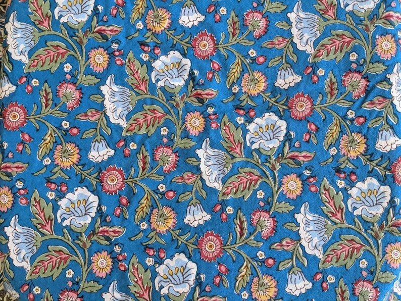 May include: A blue fabric with a floral pattern. The flowers are white, pink, and yellow. The fabric has a vintage look.