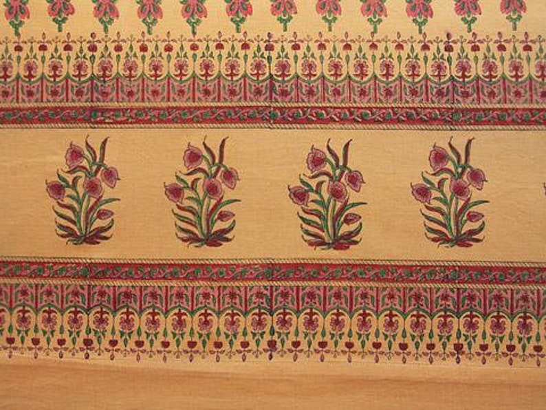 May include: A beige fabric with a repeating pattern of pink and green floral designs. The fabric has a border with a repeating pattern of pink, green, and gold.