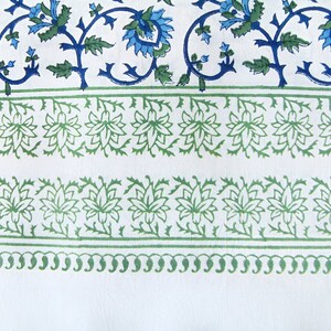 K&ouml;nnte beinhalten: Wei&szlig;er Stoff mit einem gr&uuml;nen und blauen Blumenmuster. Das Muster enth&auml;lt ein sich wiederholendes Design aus stilisierten Blumen und Bl&auml;ttern.