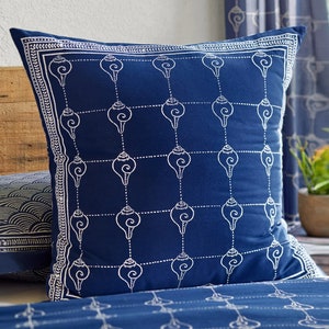 May include: A blue throw pillow with a white shell pattern. The pillow has a white border with a small, repeating pattern.