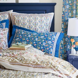 May include: A bed with a navy blue headboard and bedding featuring floral patterns in blue, white, and pink. The pillows and duvet cover display intricate designs. Two framed paintings with floral and butterfly motifs hang above the bed.