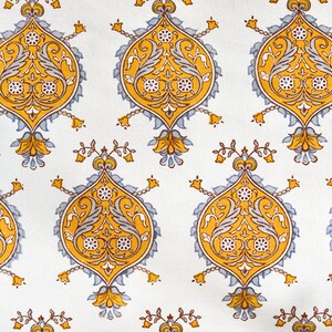 May include: A white fabric with a repeating pattern of yellow and blue floral designs. The pattern features intricate details and a traditional style.