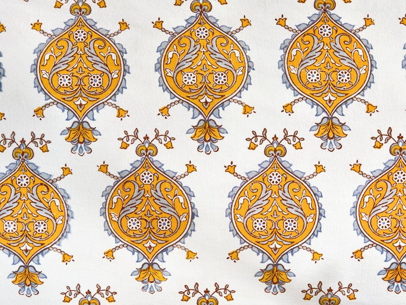May include: A white fabric with a repeating pattern of yellow and blue floral designs. The pattern features intricate details and a traditional style.