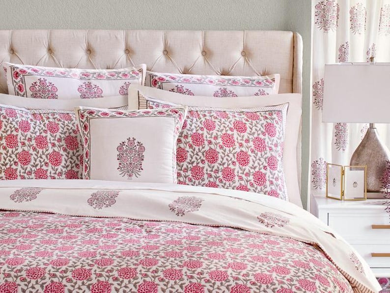 K&ouml;nnte beinhalten: Ein wei&szlig;es Bett mit einem rosafarbenen, floral gemusterten Bettbezug und passenden Kissenbez&uuml;gen. Das Bett hat ein gestepptes Kopfteil und ist mit zus&auml;tzlichen Dekokissen ausgestattet.
