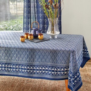 May include: A rectangular tablecloth featuring a deep blue fabric with a white repeating fan-shaped pattern, a horizontal border with white wave motifs, and a matching blue curtain with a white shell print in the background.