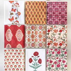 May include: Nine folded fabric squares featuring diverse patterns including butterflies, floral motifs, and geometric designs in red, orange, white, and green. A brass container, a glass jar of saffron, and two pomegranate halves are also visible.