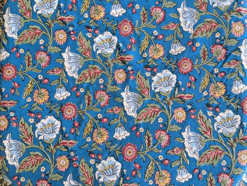 May include: A blue fabric with a floral pattern. The flowers are white, pink, and yellow. The fabric has a vintage look.