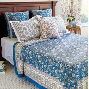 May include: A teal blue floral patterned quilt with a white border and a matching set of pillowcases. The quilt is on a bed with white sheets and a wooden headboard.