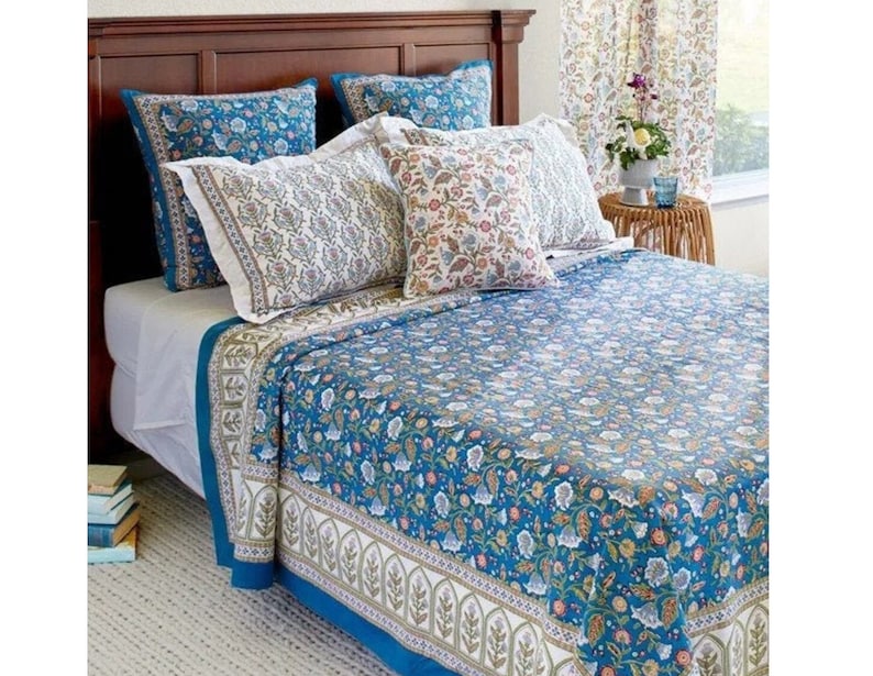May include: A teal blue floral patterned quilt with a white border and a matching set of pillowcases. The quilt is on a bed with white sheets and a wooden headboard.