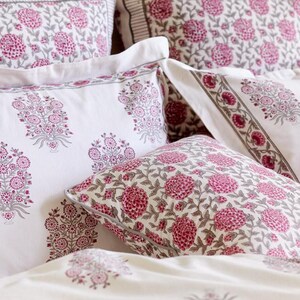 K&ouml;nnte beinhalten: Ein Set wei&szlig;er Kissenbez&uuml;ge mit einem rosafarbenen Blumenmuster. Die Kissenbez&uuml;ge sind aus einem weichen, bequemen Stoff gefertigt und weisen ein traditionelles indisches Blockdruckdesign auf.