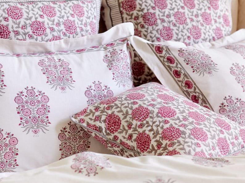 K&ouml;nnte beinhalten: Ein Set wei&szlig;er Kissenbez&uuml;ge mit einem rosafarbenen Blumenmuster. Die Kissenbez&uuml;ge sind aus einem weichen, bequemen Stoff gefertigt und weisen ein traditionelles indisches Blockdruckdesign auf.