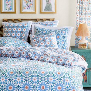 May include: A white bed with a blue and orange patterned duvet cover and matching pillowcases. The bed has a wooden headboard with a woven design. There are three framed pictures on the wall behind the bed.