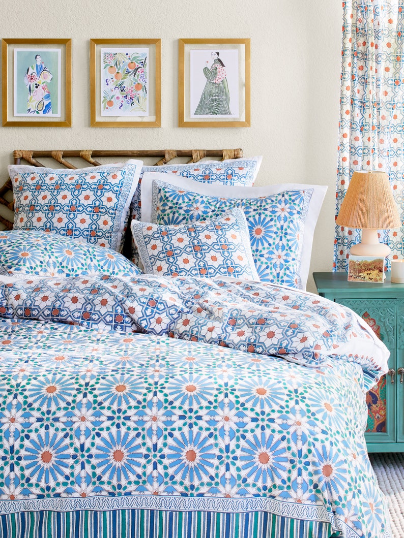 May include: A white bed with a blue and orange patterned duvet cover and matching pillowcases. The bed has a wooden headboard with a woven design. There are three framed pictures on the wall behind the bed.