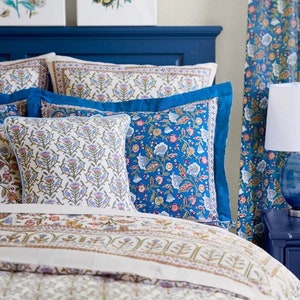 May include: A bed with a navy blue headboard and floral bedding. The bedding includes patterned pillows and a comforter with a cream background and floral designs in blue, pink, and green. Matching curtains are visible on the right.