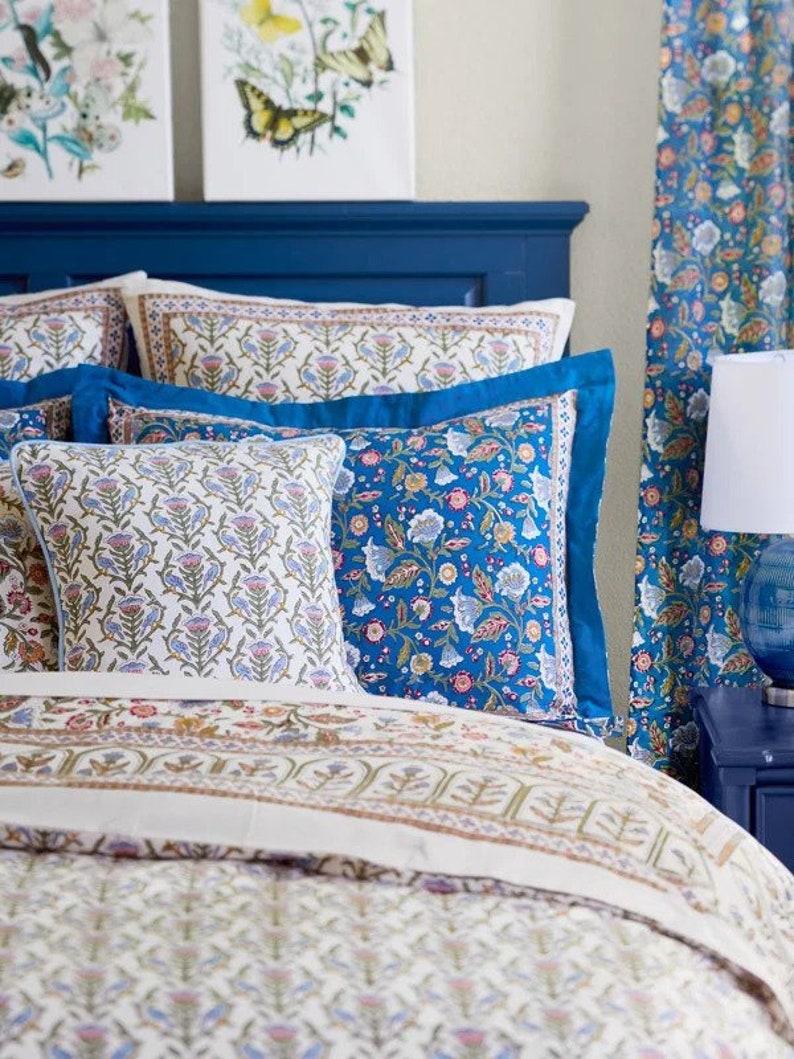 May include: A bed with a navy blue headboard and floral bedding. The bedding includes patterned pillows and a comforter with a cream background and floral designs in blue, pink, and green. Matching curtains are visible on the right.