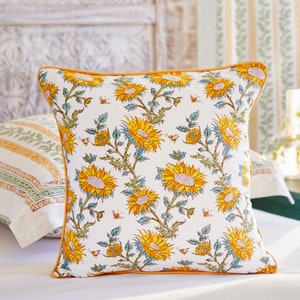 May include: A white pillow with a yellow and blue sunflower print and a yellow border. The pillow is on a white bed.