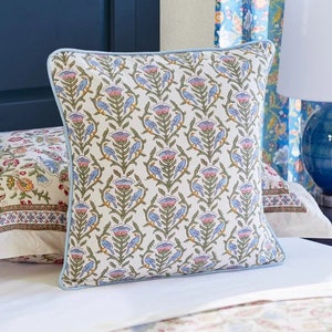 May include: A white throw pillow with a blue and pink floral pattern. The pillow has a light blue border and is sitting on a white bedspread with a floral pattern.