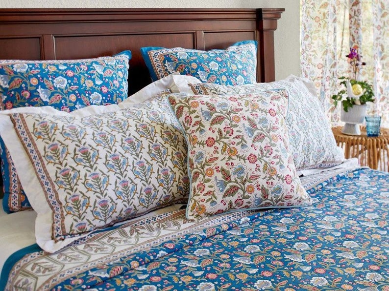 May include: A bed with a blue and white floral patterned duvet cover and matching pillowcases. There are three decorative pillows with floral patterns in shades of blue, white, and pink.